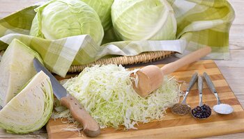 cabbage tamper, knives, spieces and cabbage heads on wooden cutting board