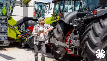 A man in a plaid shirt and cap uses a tablet while standing between large tractors. The image features a yellow leaf icon and white 4-H logo in the corners.