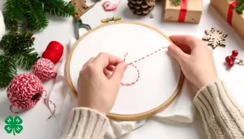 Hands preparing to embroider in a hoop, surrounded by holiday decorations and thread.