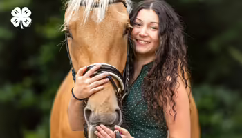 A smiling young woman posing closely with a brown horse. A green 4-H logo is in the top left corner.