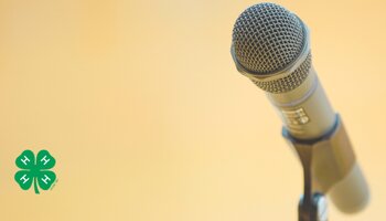 A microphone on a microphone stand on a yellow background with a green 4-H clover in the bottom left corner.