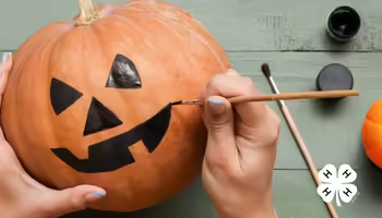 A person painting a jack-o-lantern face on a pumpkin.