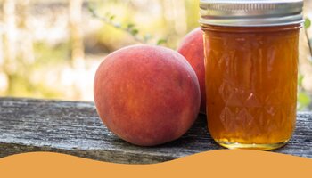 Peach jam in a jar with peaches sitting next to the jar sitting on a wooden banister.