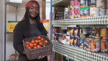 A woman holding a box of tomatoes in front of  food pantry shelf 