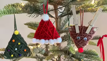 Christmas tree with three homemade yarn ornaments: a green triangular tree, a red Santa hat, and a brown reindeer face.