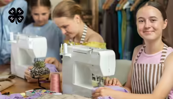 Youth working at sewing machines. A black 4-H clover in the upper left corner.