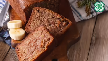 Slices of banana bread on a wooden board with fresh banana slices. A green 4-H clover in the upper right corner.