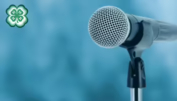 A microphone with a blue background. A green 4-H clover in the upper left corner.