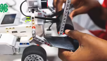A pair of hands working on a LEGO robot with wheels.
