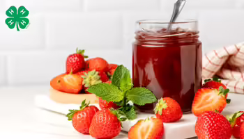 A jar of strawberry jam with strawberries on the table. A green 4-H logo in upper left corner.
