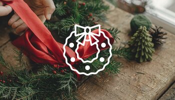 An evergreen wreath with a person tie a red bow to the top of the wreath.