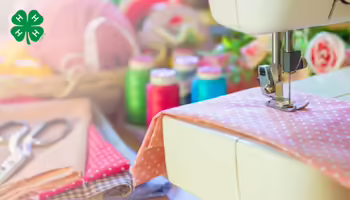 A sewing machine stitching fabric, surrounded by spools of thread, scissors, and fabric swatches, with the green 4-H logo in the upper-left corner.