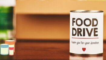 A can of food sitting on a wooden table with a white label that reads "Food Drive. Thank you for your Donation" 
