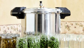 green beans in clear glass canning jars in front of astainless steel pressure canner