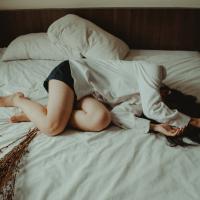 Mujer acostada en la cama cubriéndose la cara con los brazos