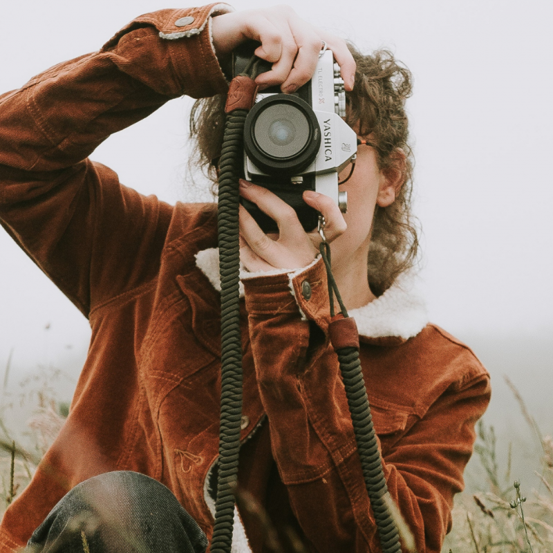 woman with brown hair taking photograph in nature with camera