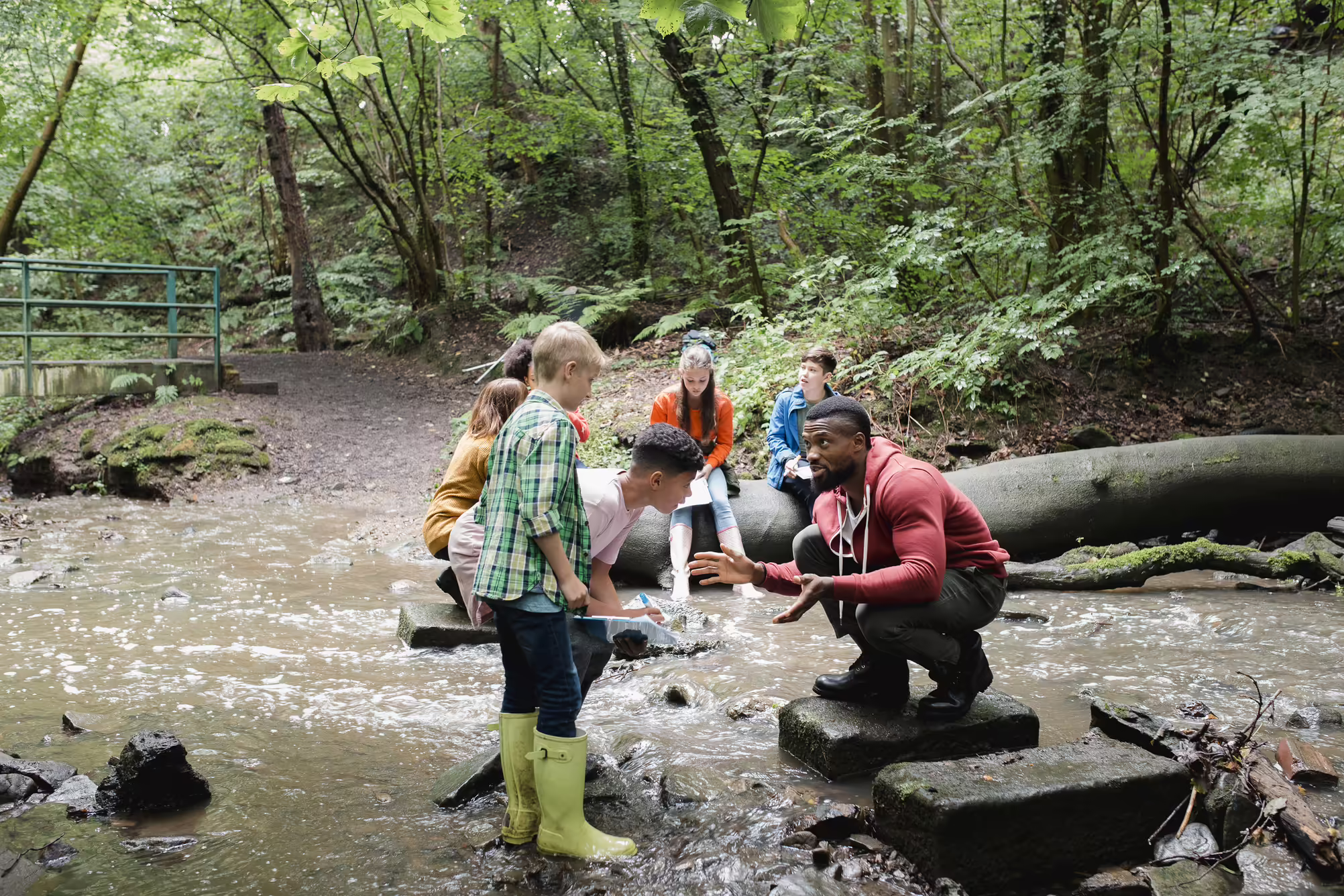 Teacher and students in wading in creek bed