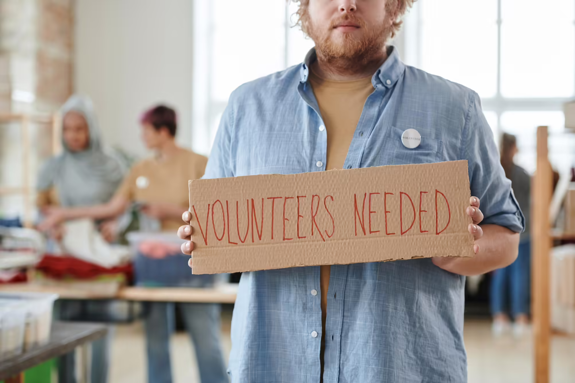 person holding sign Volunteers Needed