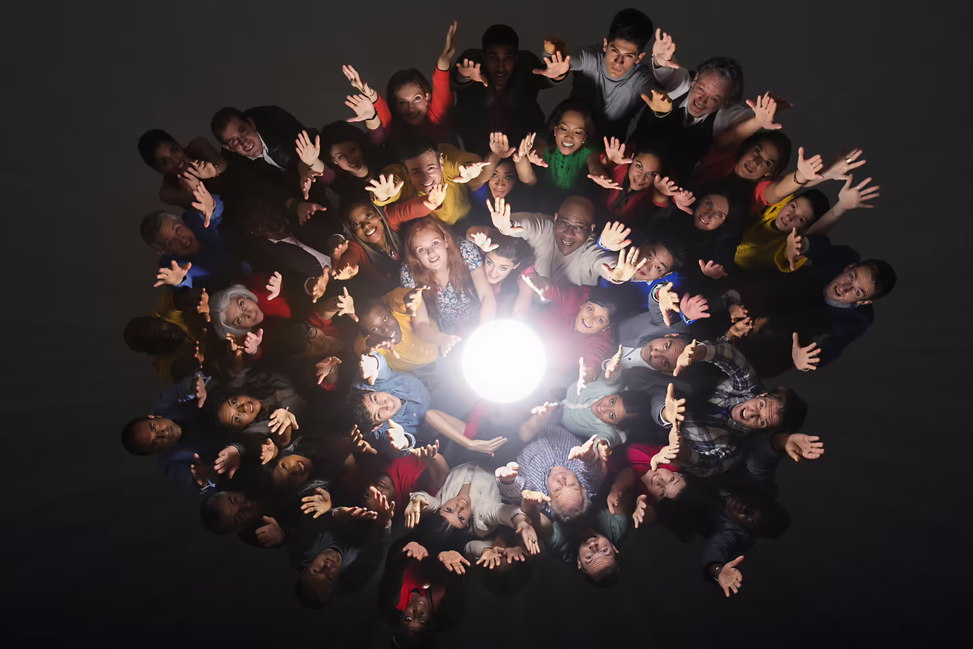 people standing in circle of light with hands in the air
