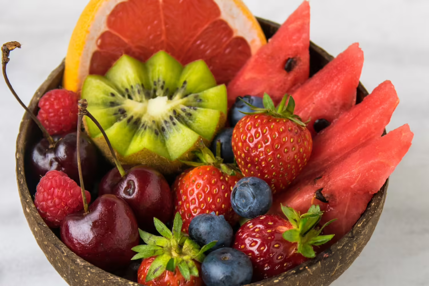 Colorful fruit in a stone bowl sitting on a white marble countertop.