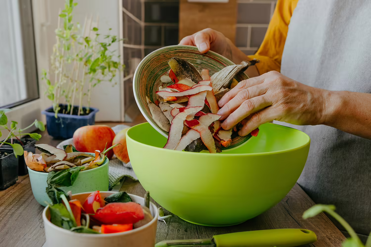 Focus on a woman's hands separating compostable materials into various containers in her kitchen.