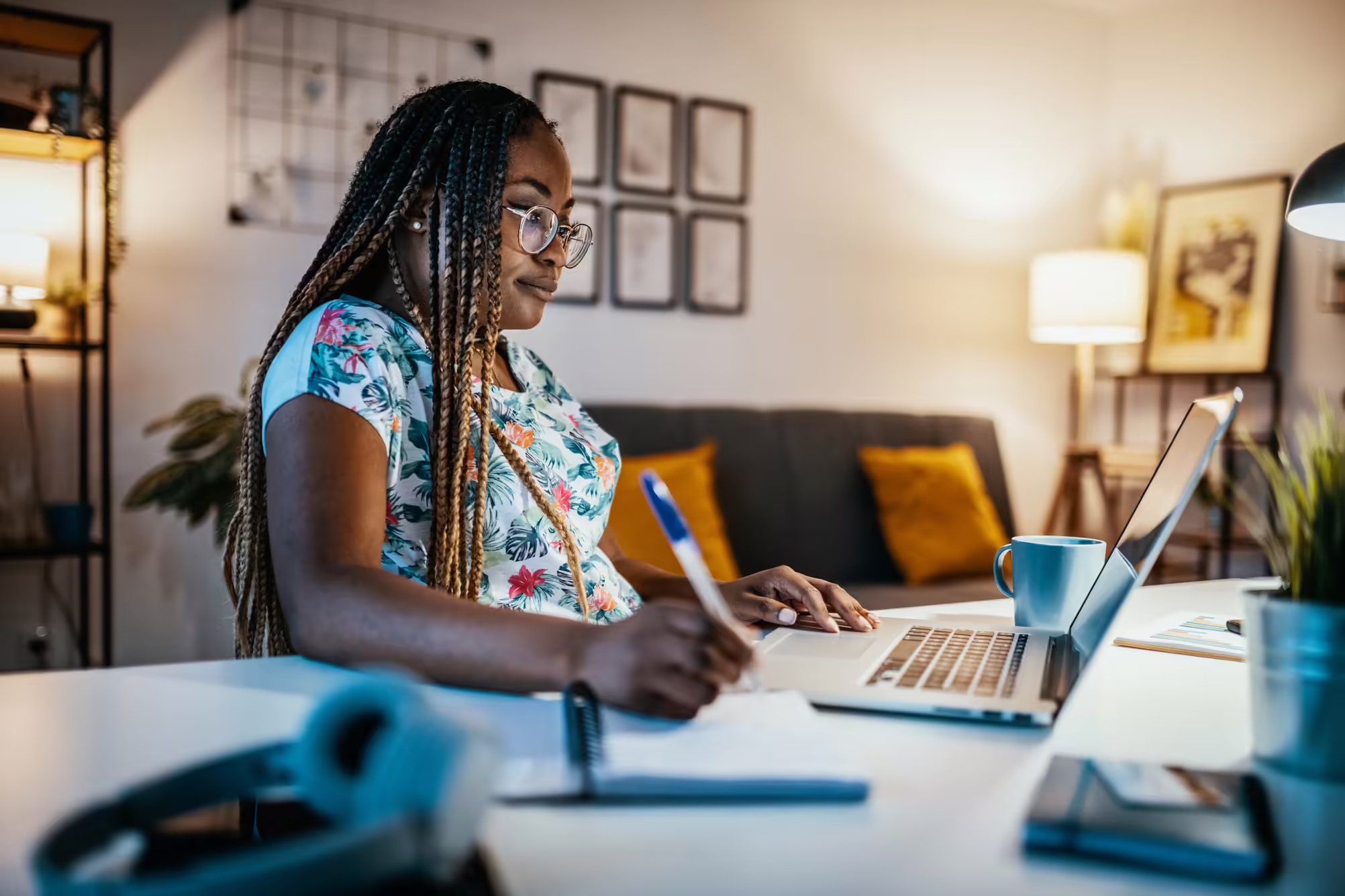 woman sitting at her desk looking at her laptop and taking notes