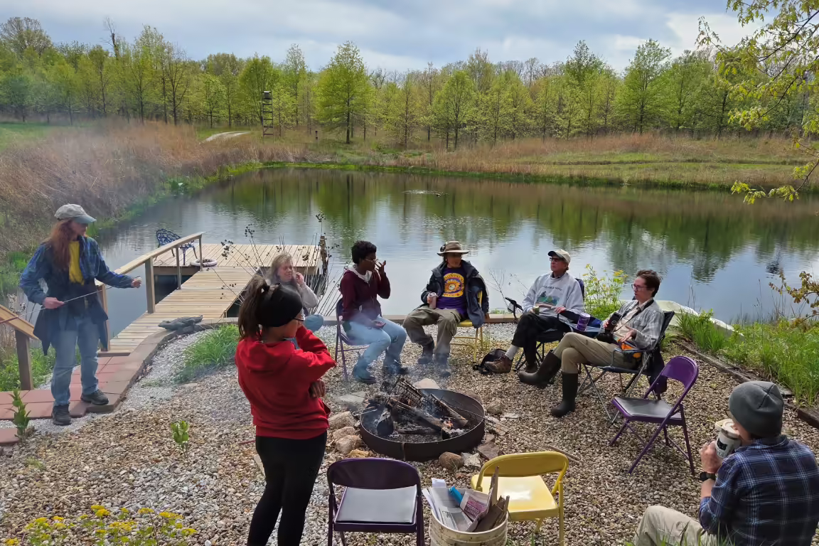 People gathered by a lakeside fire talking.