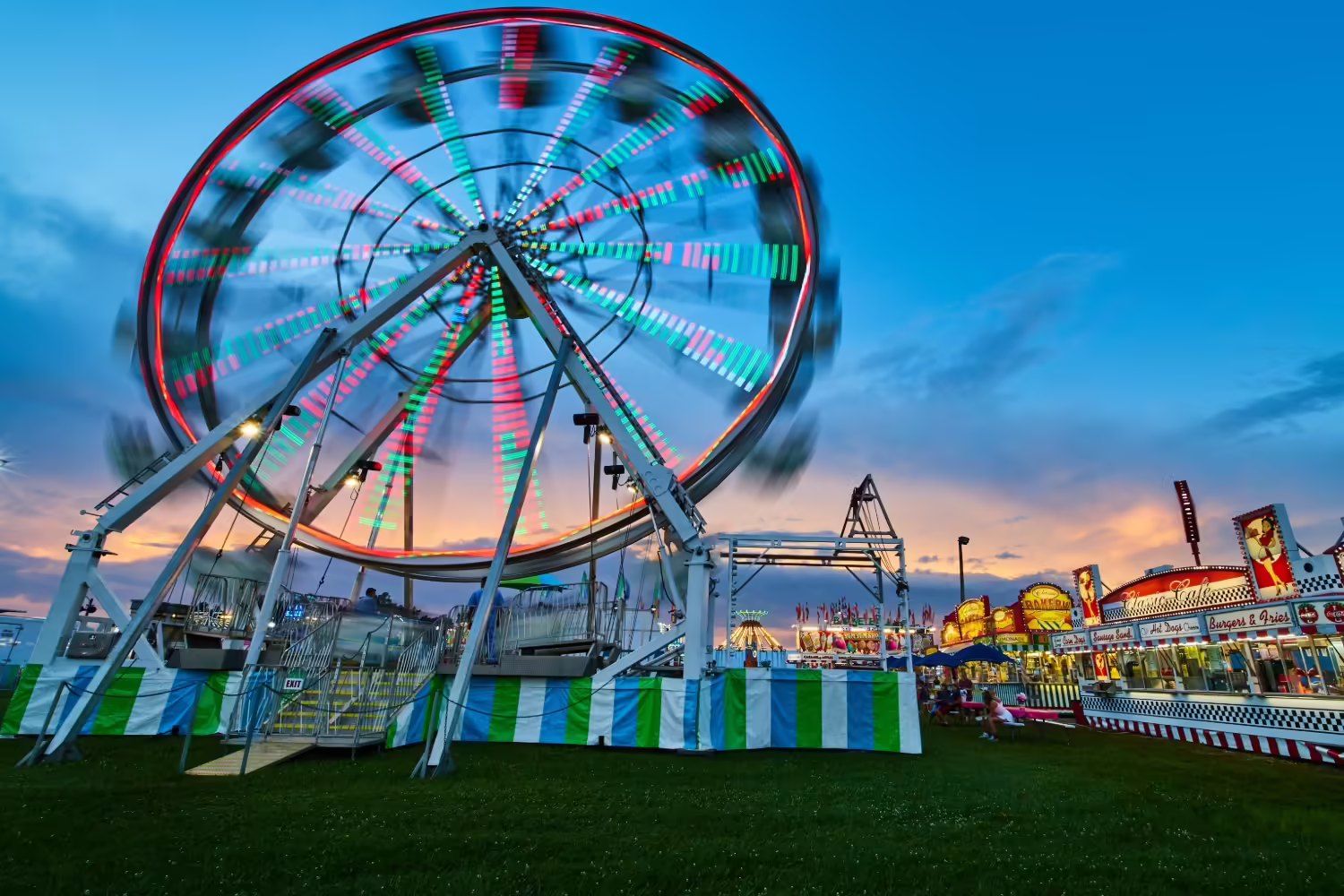 A county fair with a Ferris wheel and rides in the background 
