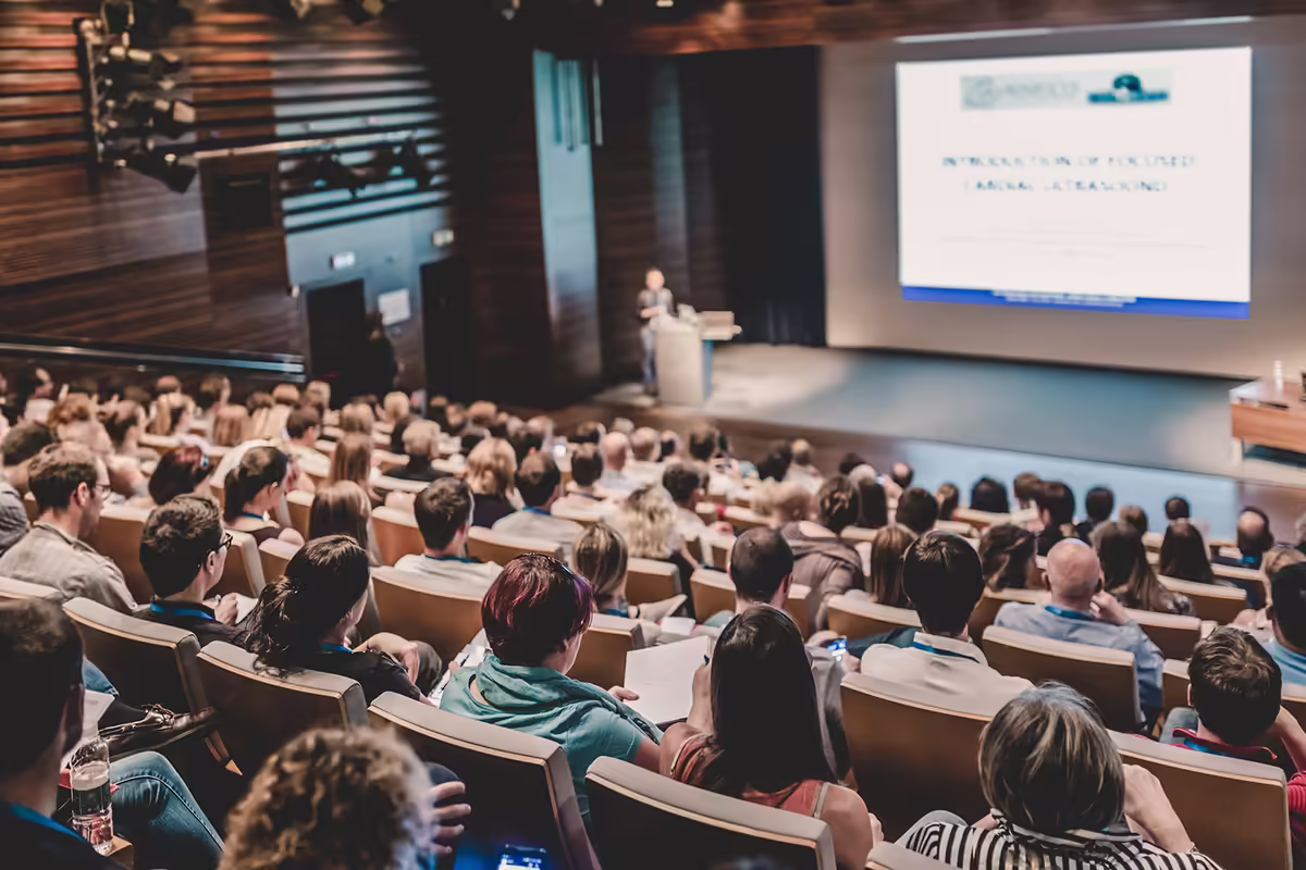 students watching a teacher present in an auditorium 
