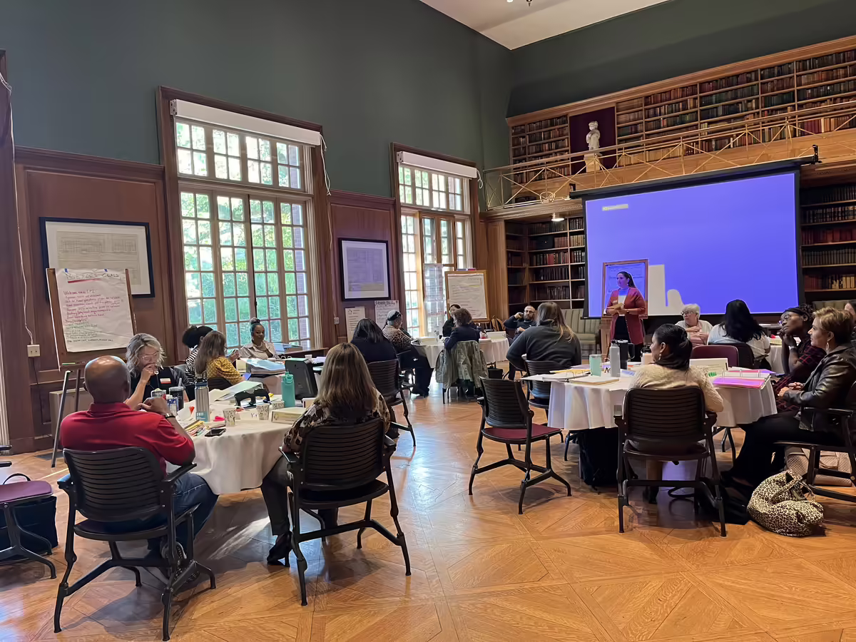 Groups of adults sitting at round banquet tables watching a slideshow training session