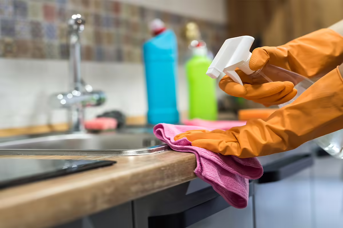 person wearing orange rubber glvoes cleaning kitchen counter