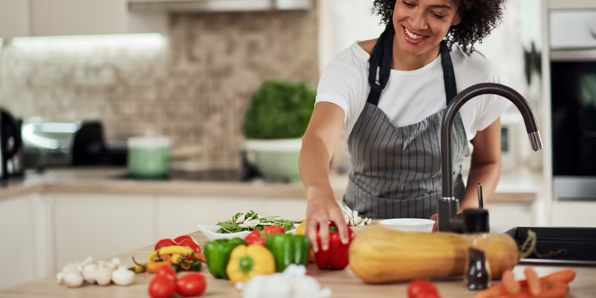 woman reaching for red pepper on kitchen counter covered with fresh vegetables