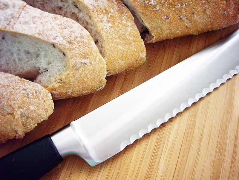 serrated knife laying on a table next to cut bread