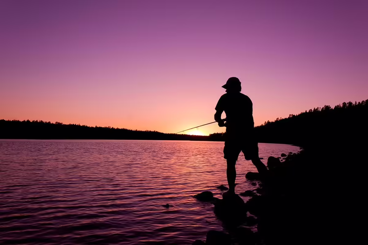 a person casts a fishing line into a lake against a setting sun