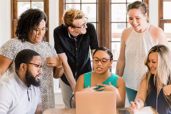 a group of people meeting around a computer