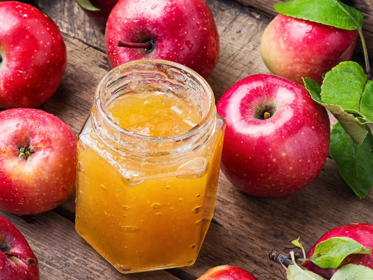 red apples around a clear jar of apple jelly