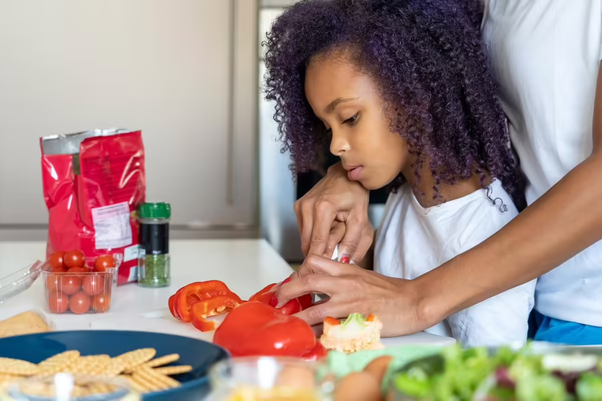 youth cutting tomatoes with help from adult