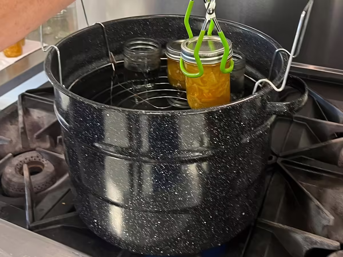 jar of processed marmelade being lifted out of a porcelain water bath canner