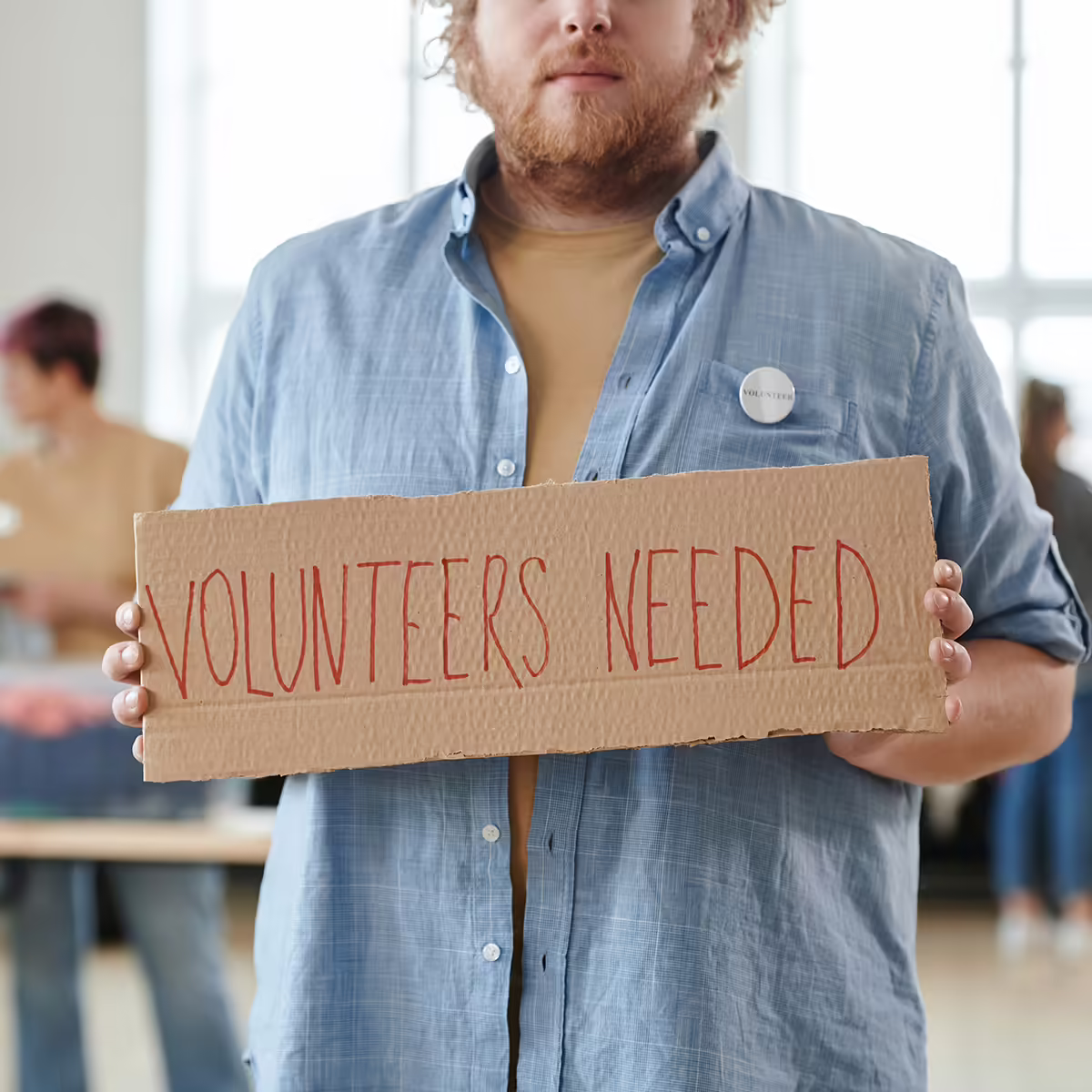 man holding volunteers needed sign