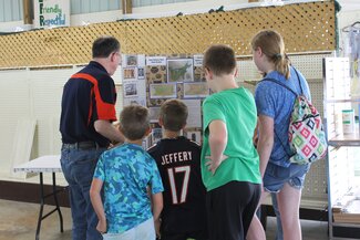 group of kids and adult standing at table looking at display board