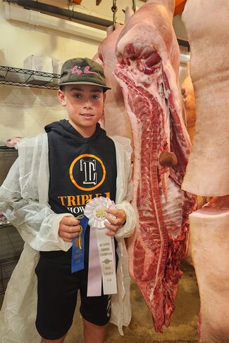 boy in baseball cap and white coat next to beef carcass