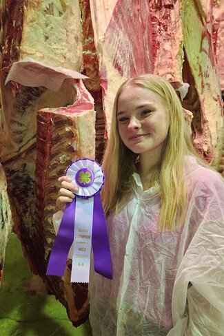 Girl with blond hair in white coat next to beef carcass