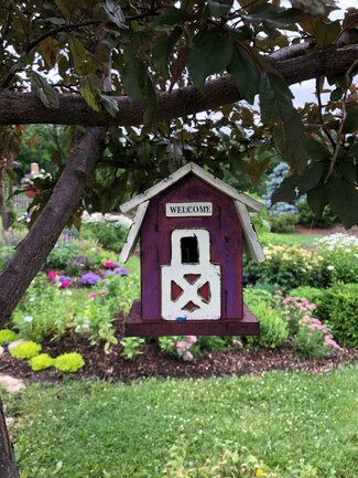 a tiny barn birdhouse in the foreground with a garden backdrop