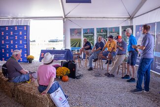 people sit on hay bales in front of a group of men on stools being interviewed