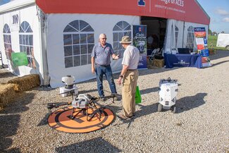 two men outside a large tent talk next to a drone on the ground