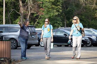 A woman directs two women in matching volunteer shirts from parking lot