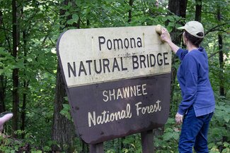 A woman washes a sign that says "pomona natural bridge shawnee national forest"