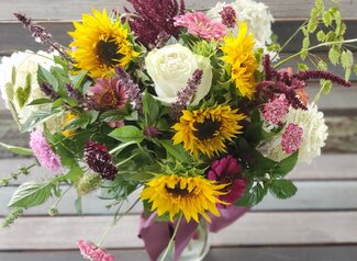 Overhead view of a vase of flowers including sunflowers, roses, and herbs.