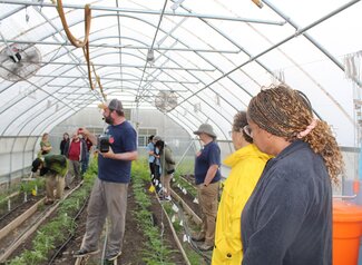 A group of people listening to a speaker in a greenhouse.