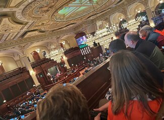 Group of people seated in a balcony viewing a state house session at the capitol.